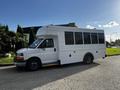 A white 2015 Chevrolet Express with large windows designed for passenger transportation parked on a street