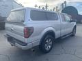 A silver 2014 Ford F-150 truck with a camper shell on the bed and alloy wheels parked in a lot