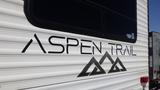 A close-up view of the side of a 2022 Aspen Trail travel trailer featuring the brand name in bold letters and a mountain graphic below it