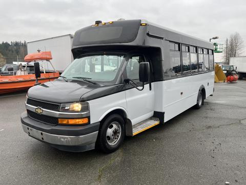 A 2018 Chevrolet Express shuttle bus with a black front and white body featuring large windows and steps at the entrance