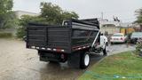 A 2021 International CV515 truck with a black dump bed positioned at an angle, showing its rear and side, equipped with a towing hitch and reflecting striping on the back