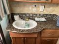 A round sink with a bottle of hand sanitizer and a water bottle on a granite countertop inside a motorhome with wood cabinetry and a backsplash of small tiles