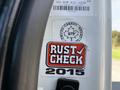 A close-up of a sticker on a vehicle door featuring the text RUST CHECK 2015 in bold red and black letters with a white background