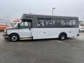 A white and gray 2017 Chevrolet Express bus with large windows and a high roof parked on a roadway