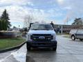 A 2017 Ford F-350 SD with a black front grille and headlights is parked in a lot with a flatbed attachment and an orange safety light on the roof