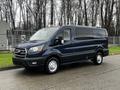 A 2020 Ford Transit in dark blue with a spacious passenger area and silver wheels parked on a pavement