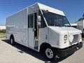 A white 2012 Ford Econoline delivery van with a large cargo area and a side door is parked with its front angled towards the viewer