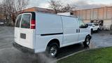 A white 2005 Chevrolet Express van with a high roof and chrome wheels parked at an angle with steam rising from the ground around it