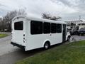 A white 2017 Chevrolet Express bus with large windows and an open side door parked on a grassy area