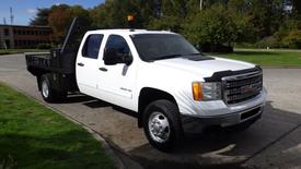 A white 2014 GMC Sierra 3500HD with a flatbed and an orange beacon light on the roof parked on a street