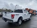 A white 2017 Ford F-150 parked with its bed and tailgate visible featuring a 4x4 badge and chrome accents on the rear bumper and side steps