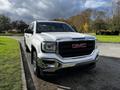 A white 2017 GMC Sierra 1500 pickup truck is parked with a chrome front grille displaying the GMC logo and shiny alloy wheels