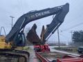 A 2014 John Deere 350G excavator with a large bucket raised is positioned over a trailer in a construction setting