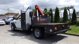 A white 2014 RAM 5500 flatbed truck with a rear-mounted crane and a metal tool compartment on the side