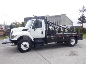 A 2013 International 7300 flatbed truck with a black bed and hydraulic crane on the side parked on a concrete surface