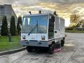 A 2007 Tennant Sentinel street cleaning vehicle with a white exterior and large windows is positioned on paved ground, showcasing its compact design and operational lights