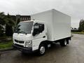 A 2012 Mitsubishi Fuso FE delivery truck with a white box cargo area and orange roof lights parked at an angle