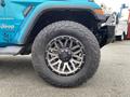 A close-up of a blue 2020 Jeep Wrangler's wheel and tire showcasing a multi-spoke alloy rim and rugged tread design