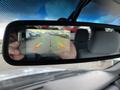 Rearview mirror displaying a backup camera image of a parking lot with various vehicles lined up and guide lines for parking assistance