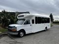 A white 2017 Chevrolet Express shuttle bus with large windows and a raised roof parked on a pavement