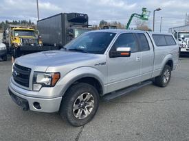 A silver 2014 Ford F-150 with a prominent grille and a functional bed cap positioned in the foreground