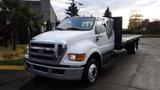 A 2008 Ford F-650 with a flatbed in the foreground featuring a white exterior and chrome accents