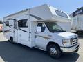 A white 2012 Ford Econoline with a large camper shell and sloping roof, featuring side windows and decorative graphics on the exterior