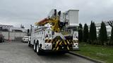 A 2006 International 7500 bucket truck with a yellow boom arm and a white utility body parked at an angle displaying its rear and lifted bucket assembly