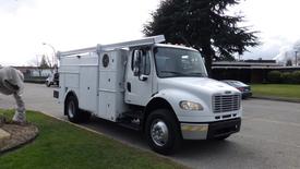 A white 2006 Freightliner M2 106 Medium Duty truck with a utility body and equipment compartments on the side