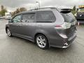 A 2013 Toyota Sienna minivan in gray parked at an angle showing its side and rear details including alloy wheels and taillights