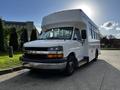 A 2015 Chevrolet Express bus with a white exterior featuring large windows and a prominent front grille parked with a clear view of its front and side