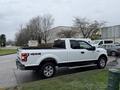 A white 2018 Ford F-150 pickup truck parked on a street with a black truck bed and 4x4 decal on the rear side