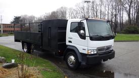 A white 2009 International CF 600 truck with a flatbed and a large black cargo area attached to its rear