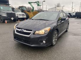 A 2014 Subaru Impreza in dark gray with distinctive headlights and sleek lines parked on a wet surface