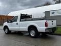 A white 2011 Ford F-250 Super Duty pickup truck with an open bed and metal tool racks is parked with its profile facing slightly towards the viewer