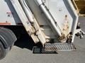 2010 Freightliner MT45 Garbage Truck with visible hydraulic lift arms and a metal step platform on the rear side