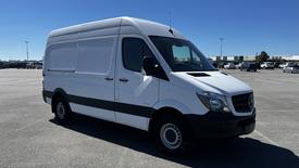 A 2016 Mercedes-Benz Sprinter van with a white exterior and black accents parked in an open area