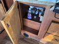 A wooden cabinet with an open door revealing shelves containing various bottles and a small container inside