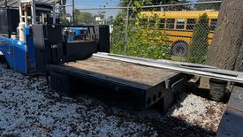 A 2000 Service Flat Deck 8 Foot truck bed with a flat surface and side panels positioned near a tree and a visible fence