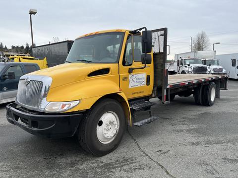 A yellow 2007 International 4300 flatbed truck with a black grille and side steps is parked with its door open