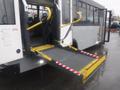 A yellow wheelchair ramp extending from the rear of a 2016 Chevrolet Express bus with black side panels and gray flooring