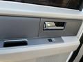 A close-up of the interior door panel of a 2013 Ford Expedition featuring a plastic handle a small window control and a textured surface
