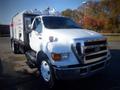 A white 2006 Ford F-650 truck with a large black and white box attached to the rear and orange lights on top