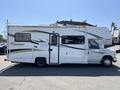 A white 2012 Ford Econoline RV with a gray and black stripe design and the word Coachmen written on the side