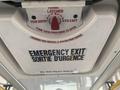 A ceiling-mounted emergency exit sign in a vehicle indicating how to open the hatch with instructions in English and French