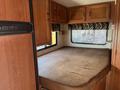 Interior of a 2012 Ford Econoline featuring a bed with a brown mattress and wooden cabinetry above it with a patterned window covering