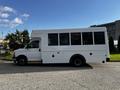 A white 2015 Chevrolet Express bus with multiple windows on the side parked on a paved surface