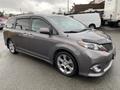 A gray 2013 Toyota Sienna minivan with sleek lines and alloy wheels parked at a location with wet pavement