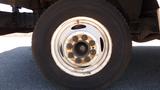 A close-up of a white wheel rim with rusted bolts and a black tire from a 2006 Ford Econoline