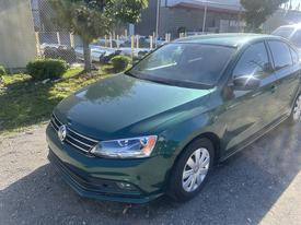 A green 2017 Volkswagen Jetta parked with a shiny exterior and a simple front grille design featuring the Volkswagen logo on the center